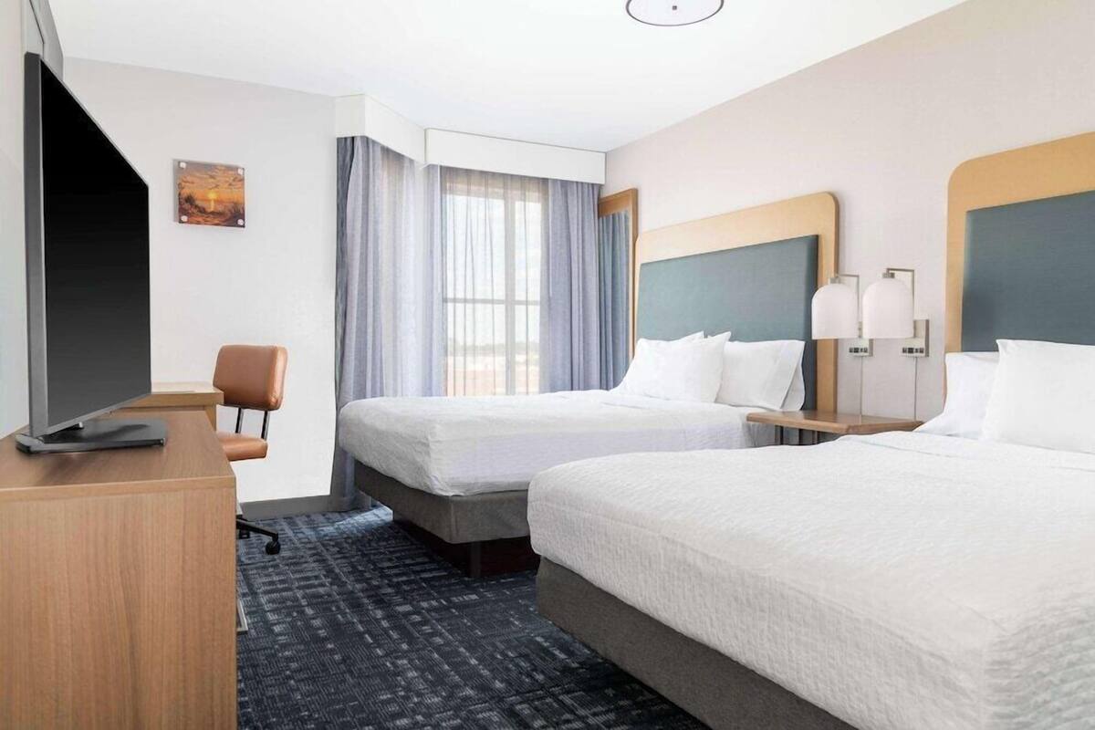 A hotel room with two beds, a desk, a chair, a TV, and a window with curtains.