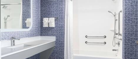 A modern bathroom with a white sink, a bathtub with grab bars, and a shower with a handheld showerhead.