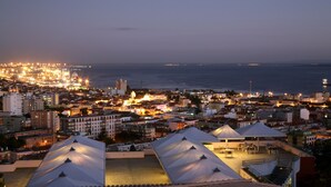 Un paisaje urbano costero al anochecer, con edificios iluminados y vistas al mar.