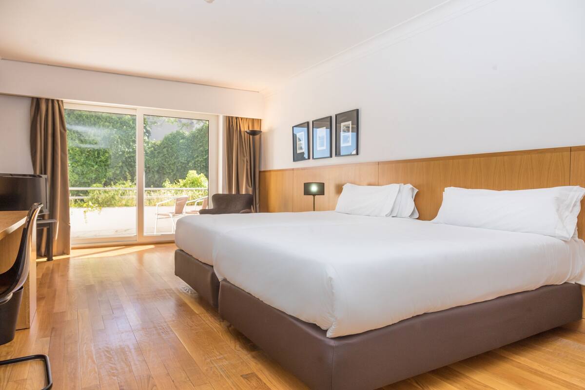 Une chambre d’hôtel avec un grand lit, un bureau, une chaise et une vue sur l’extérieur grâce à une porte coulissante.