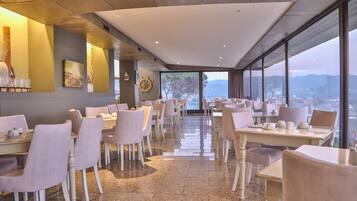 A modern dining area with tables and chairs, large windows with a view, and a ship's wheel decoration on the wall.