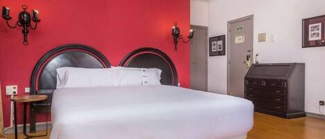 Une chambre d’hôtel avec un lit, une petite table, deux lampes fixées au mur, une commode et une porte.