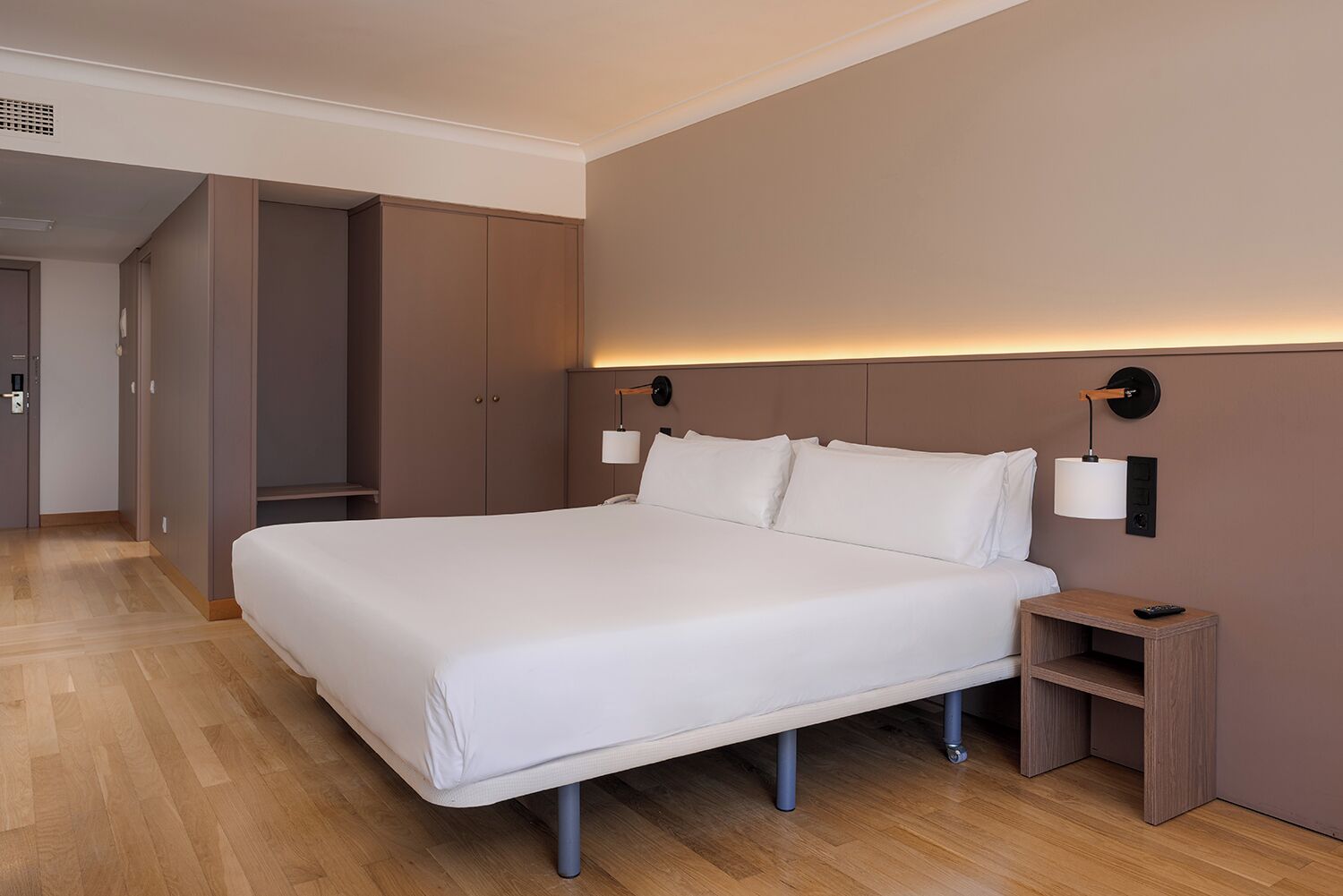 A modern hotel room with a large bed, bedside tables, and built-in wardrobes.