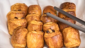 Una bandeja de pasteles recién horneados, posiblemente croissants, con un par de pinzas encima.