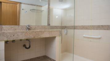Un baño con ducha de vidrio, encimera de mármol y mueble de madera.