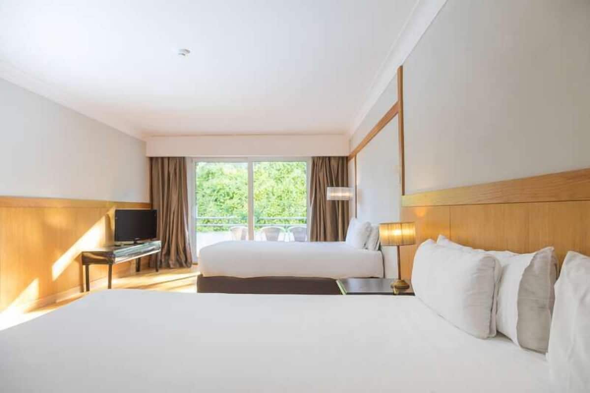 Une chambre d’hôtel avec un grand lit, un bureau avec une télévision et une fenêtre avec des rideaux.