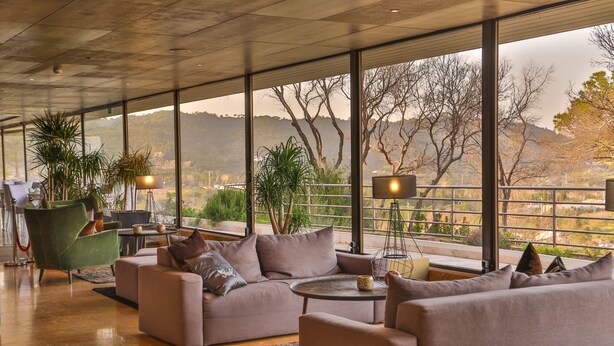 Una sala de estar moderna con un conjunto de sofá, una mesa de centro y vistas a un paisaje montañoso a través de grandes ventanales.