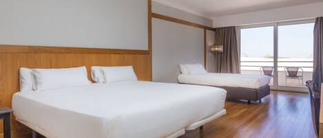 A hotel room with two beds, a wooden headboard, a large window with a view, and a balcony with wicker chairs.