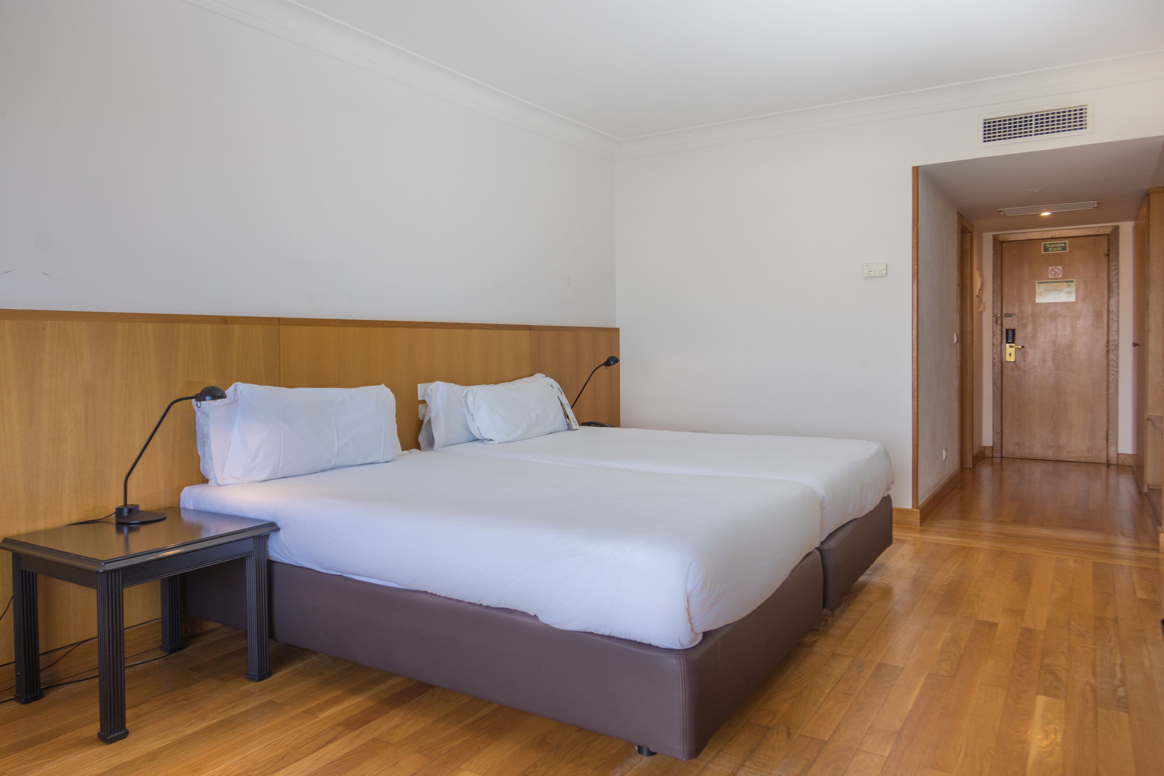 A hotel room with a double bed, a bedside table, and a wooden headboard.