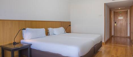 A hotel room with a double bed, a bedside table, and a wooden headboard.