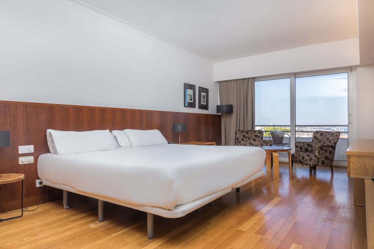 Une chambre d’hôtel avec un grand lit, une petite table, une chaise et un balcon avec vue.