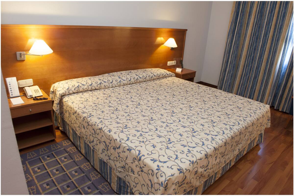 Une chambre d’hôtel avec un grand lit, deux lampes de chevet, un téléphone, une table de chevet et un tapis à motifs.