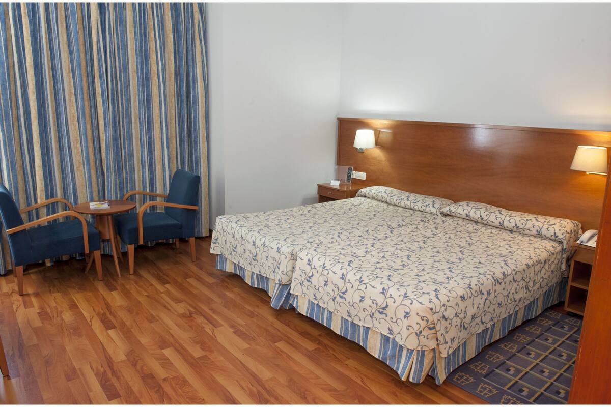 Une chambre d’hôtel avec un grand lit, un bureau avec une chaise, une table de chevet avec une lampe et un rideau.