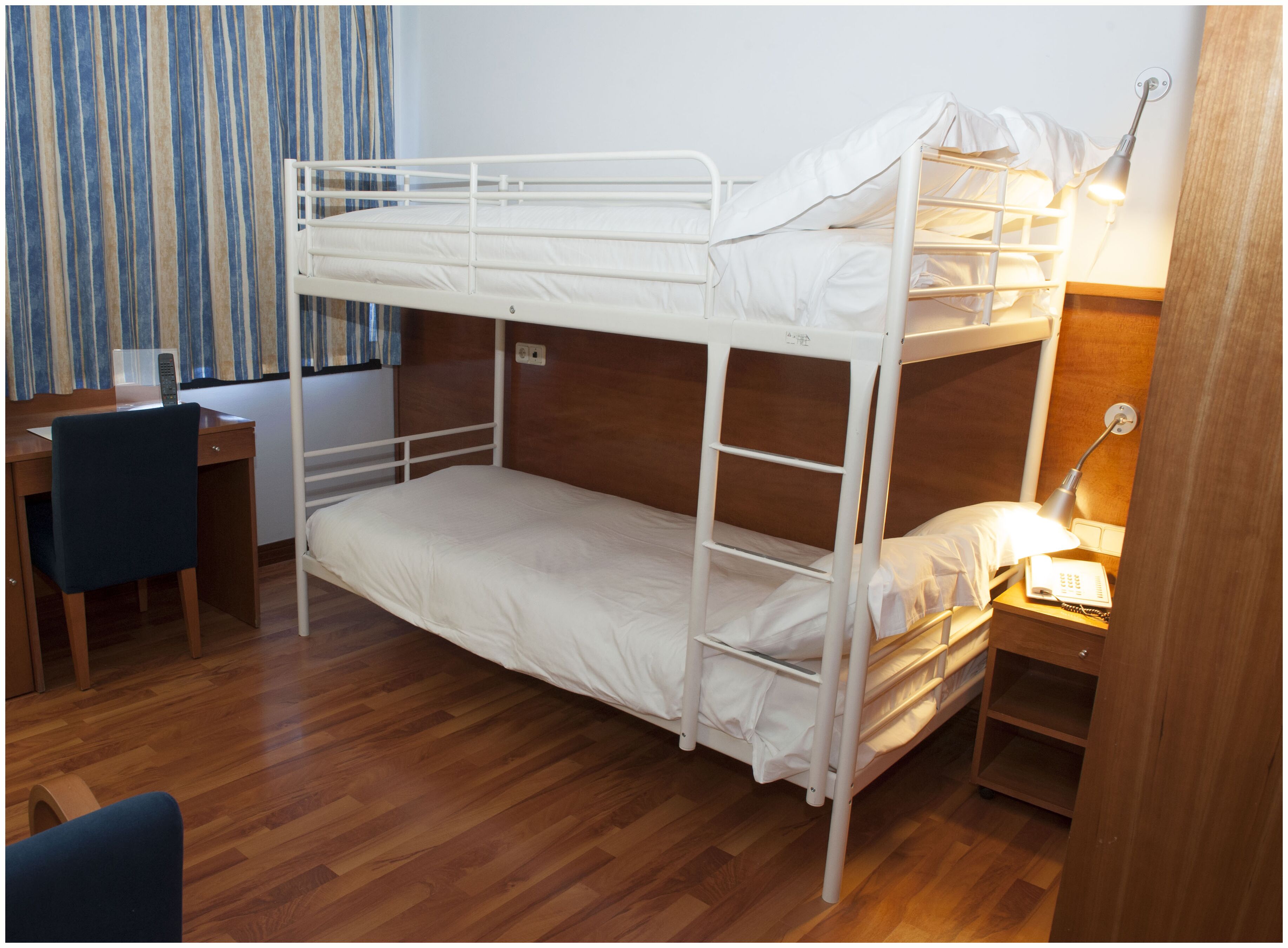 Una cama litera con escritorio y silla, una lámpara de noche y una mesita de madera.