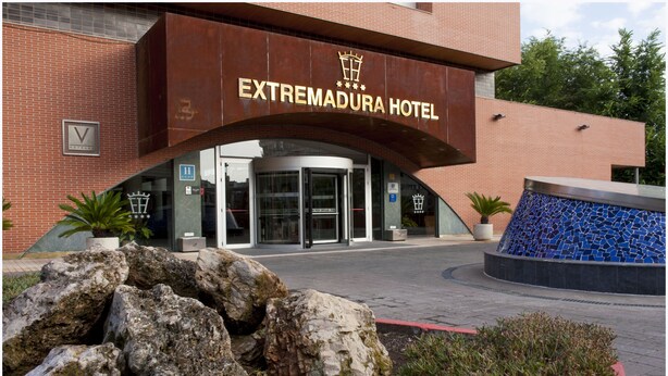 Entree van Hotel Extremadura met een modern design, met een opvallend bord, een draaideur en een decoratieve blauwe mozaïekfontein.