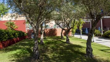 Un patio con árboles, un muro rojo y un edificio con un letrero al fondo.
