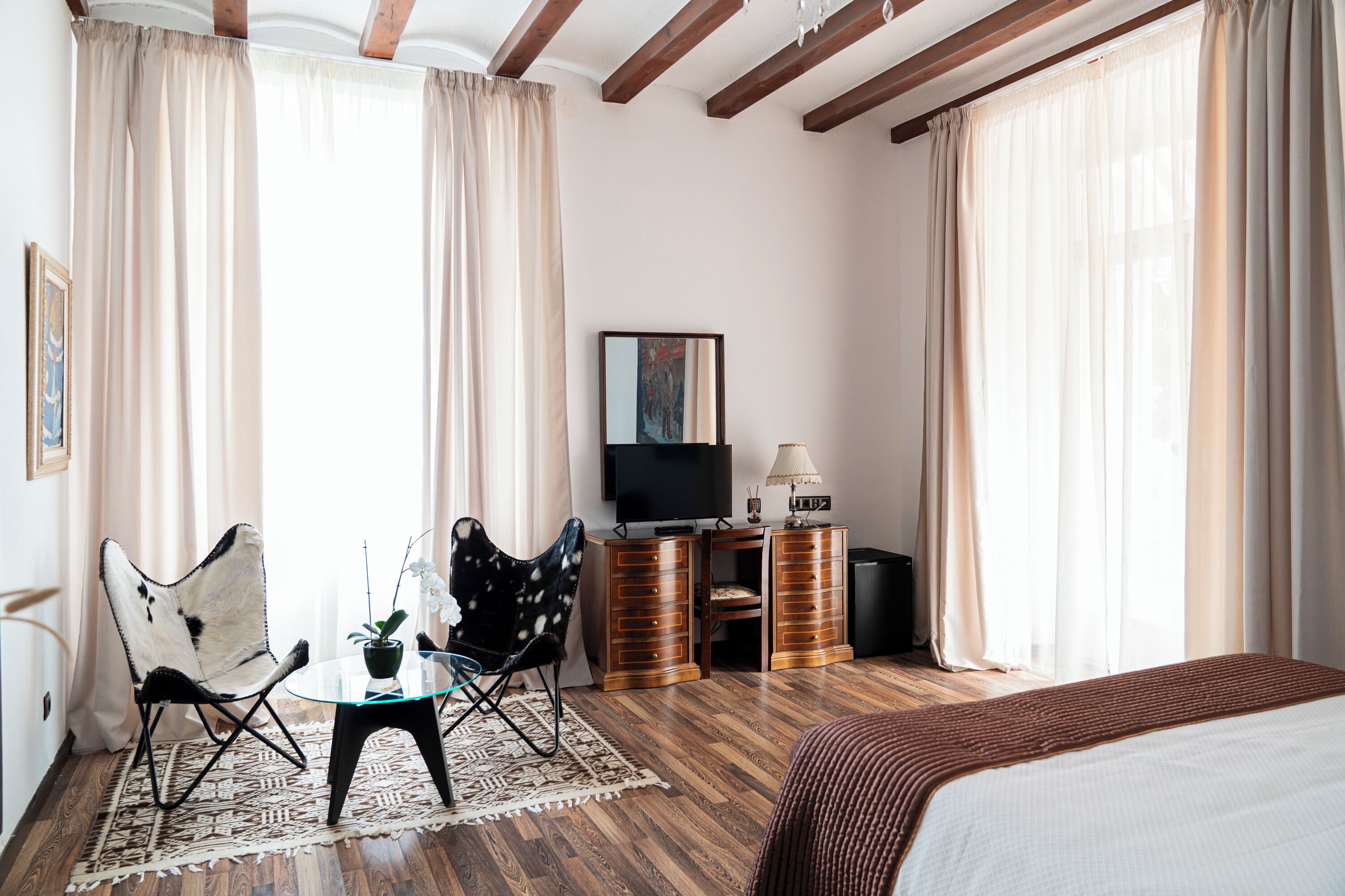 Ein Hotelzimmer mit Bett, Fernseher, Schreibtisch, Stuhl und einem Fenster mit Vorhängen.