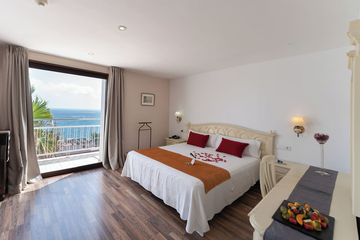Ett hotellrum med en stor säng, ett sängbord, en liten avlastningsyta, ett skrivbord och utsikt över havet.