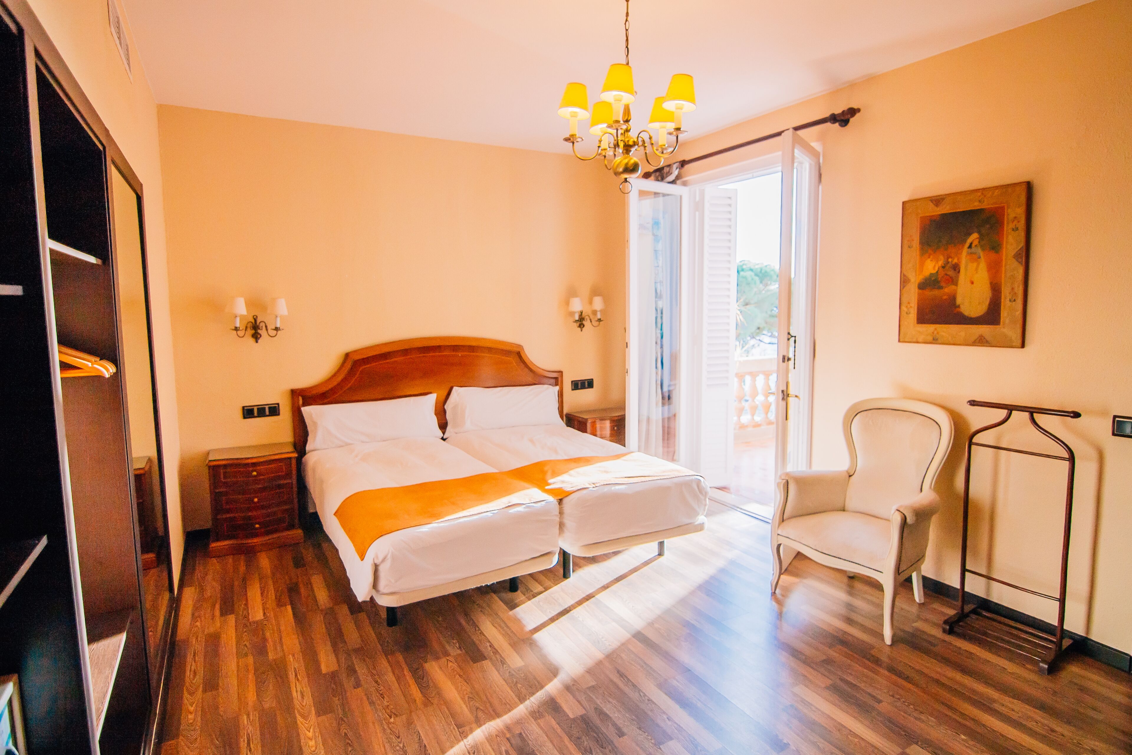 Una habitación de hotel con suelo de madera, una cama doble, una silla, un armario y un cuadro en la pared.