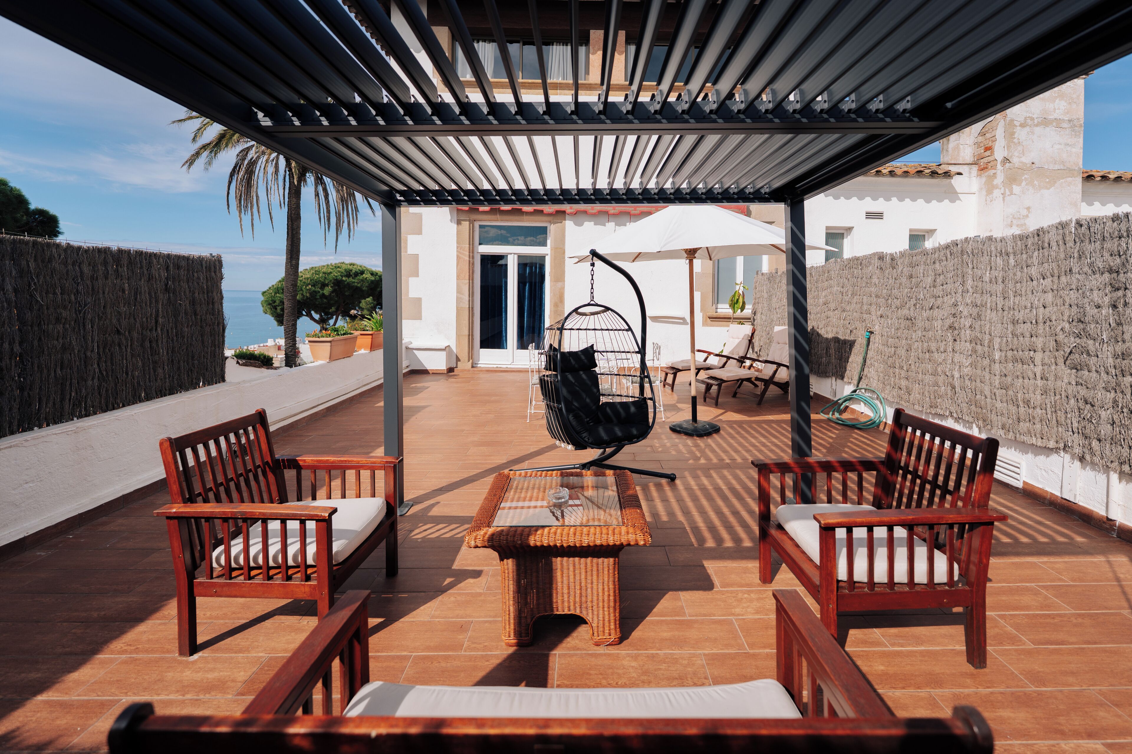 A covered outdoor seating area with wicker furniture and a hanging chair, overlooking a scenic view.
