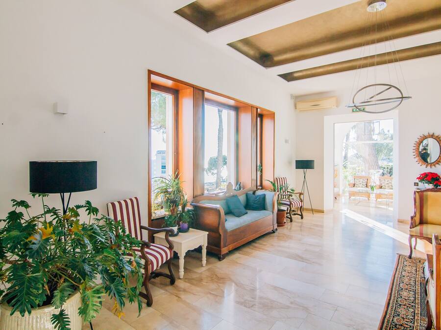 Amplia sala de estar con sofá, sillones y una mesa de centro. Grandes ventanales permiten la entrada de luz natural y ofrecen vistas al exterior.