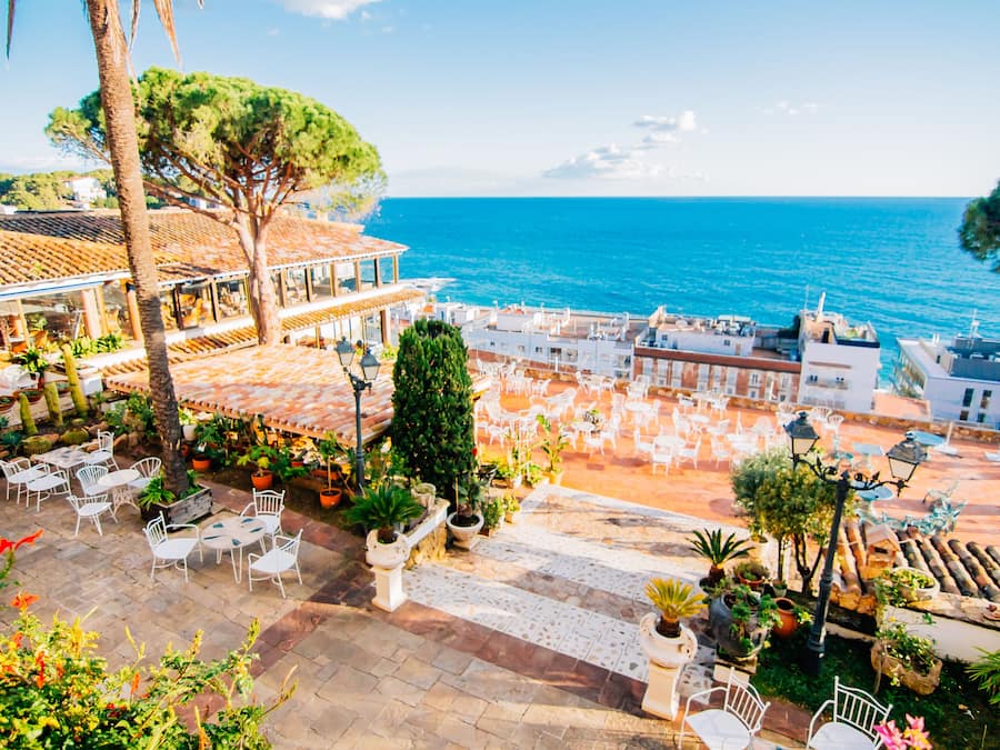 Una terraza costera con mobiliario exterior, plantas en macetas y vista al mar.