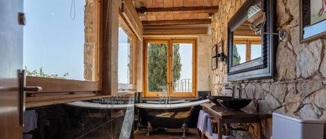 A bathroom with a stone wall, wooden beams, a large window, and a bathtub.