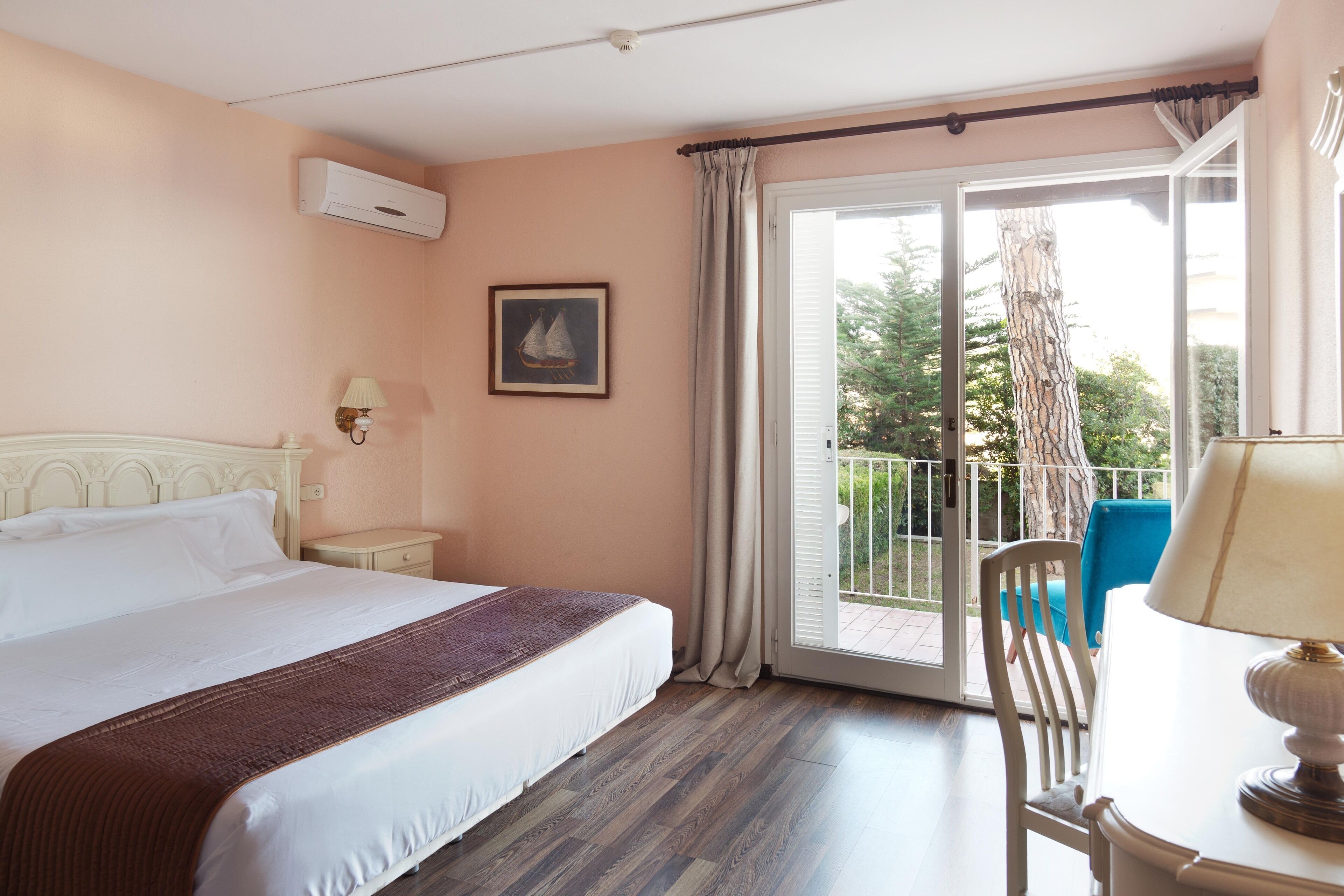 Un dormitorio con cama, mesita de noche, lámpara, silla y balcón con vista a árboles.
