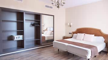 A hotel room with a large wardrobe, a bed with white linens, a wooden headboard, and a chandelier.