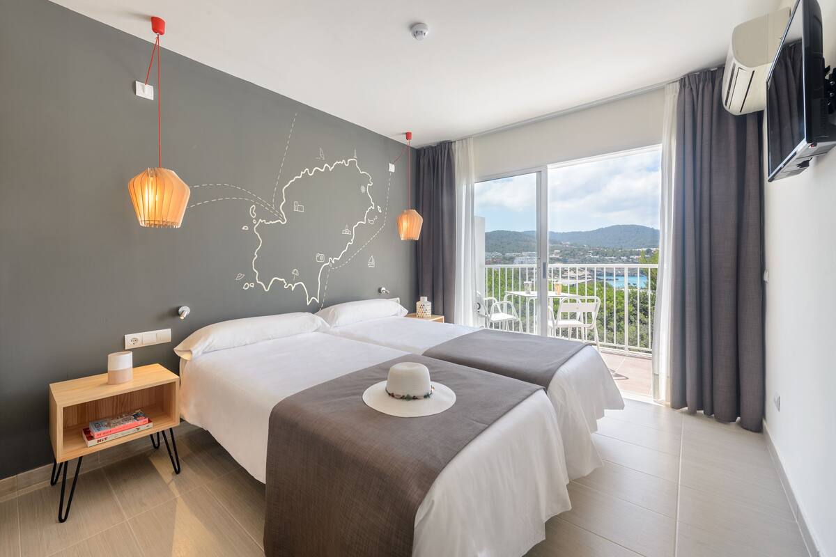 A hotel room with two beds, a map on the wall, a balcony with a view, and a television on the wall.