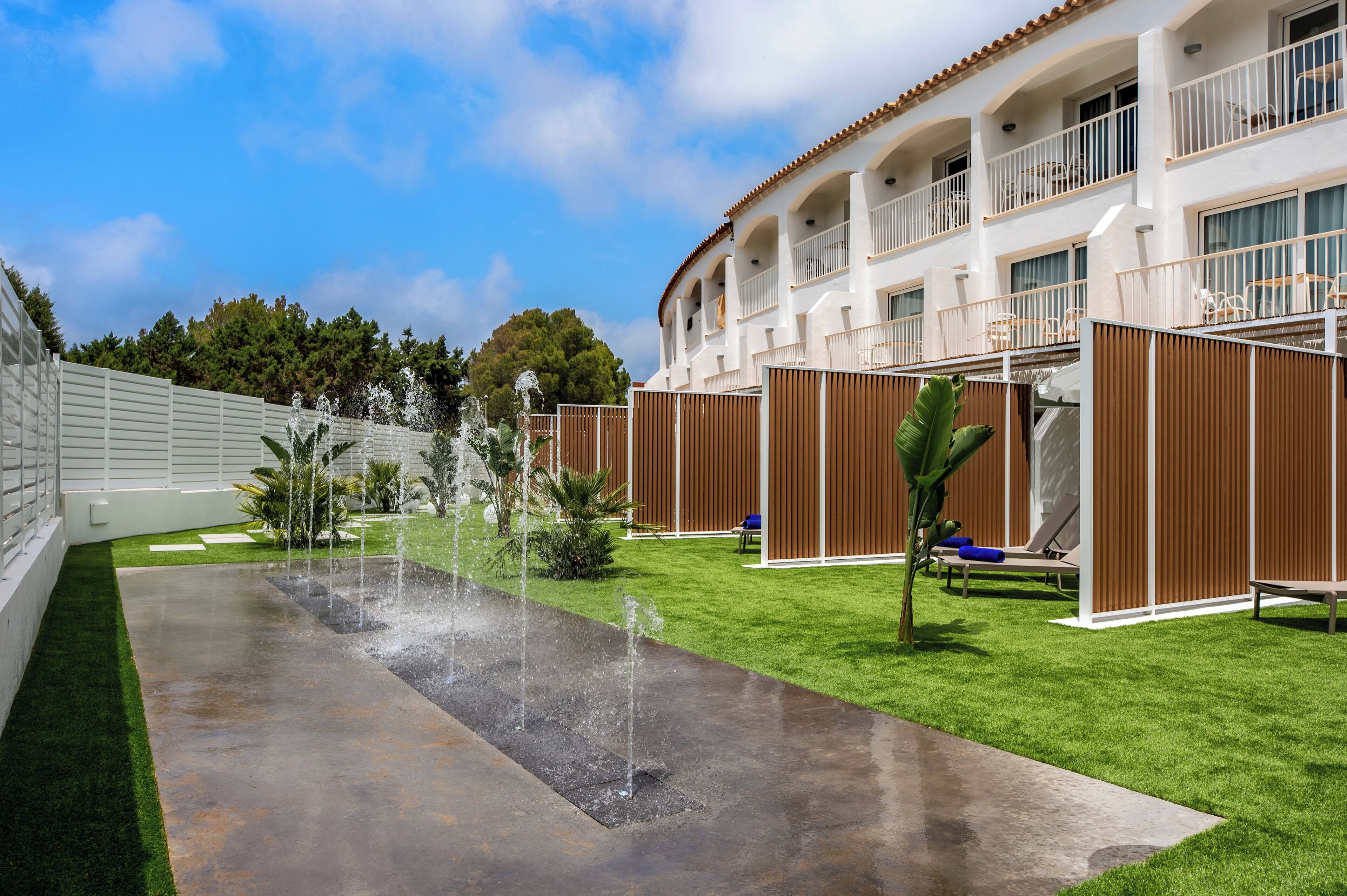 Een hotel binnenplaats met een waterpartij, een groen gazon en terrasstoelen.