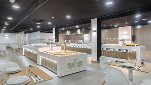 A modern restaurant with a central island, multiple seating areas, and a clean, contemporary design. - Hotel Vibra Cala Tarida (Sant Josep de sa Talaia)