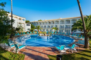 Un espace piscine avec des chaises longues, des palmiers et un bâtiment doté de balcons.