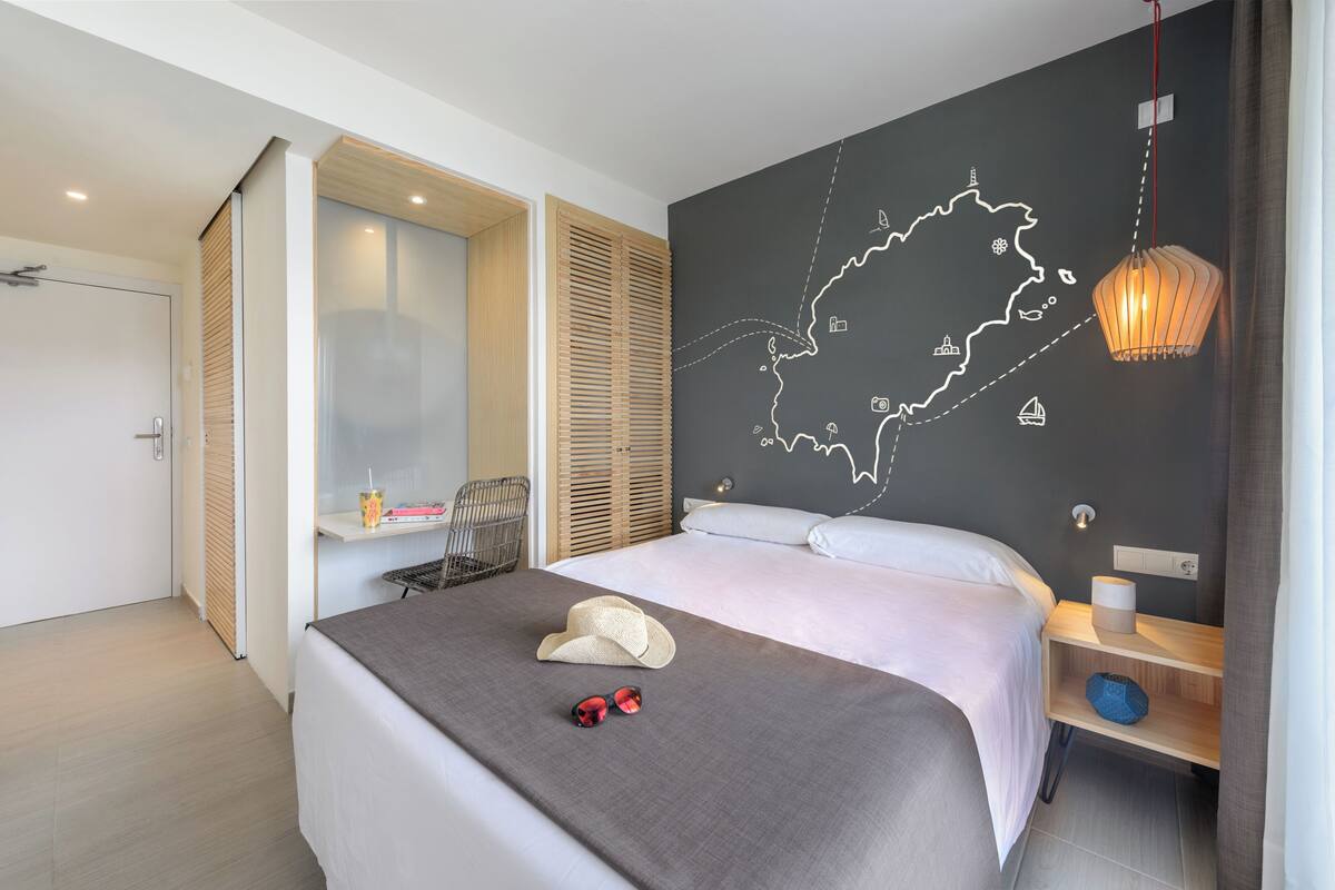 A modern hotel room with a large bed, a map on the wall, a wooden nightstand, and a window with blinds.