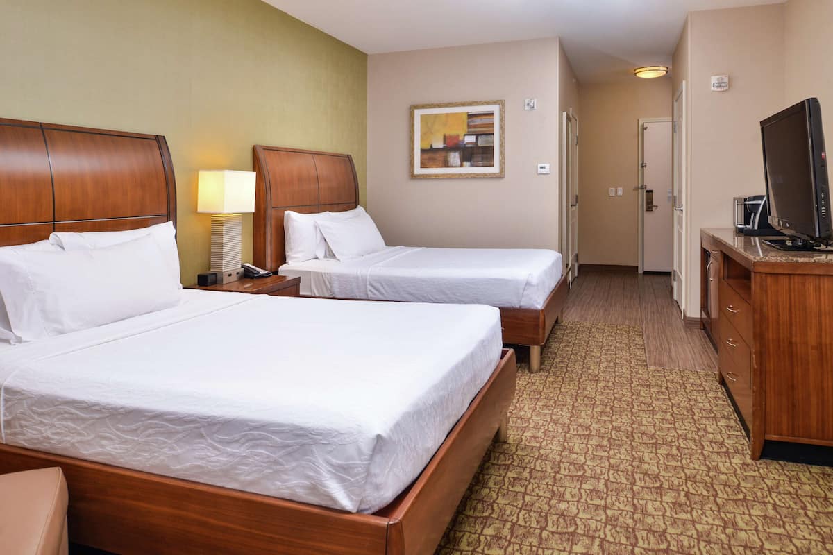 A hotel room with two beds, a television, a desk with a lamp, and a painting on the wall.