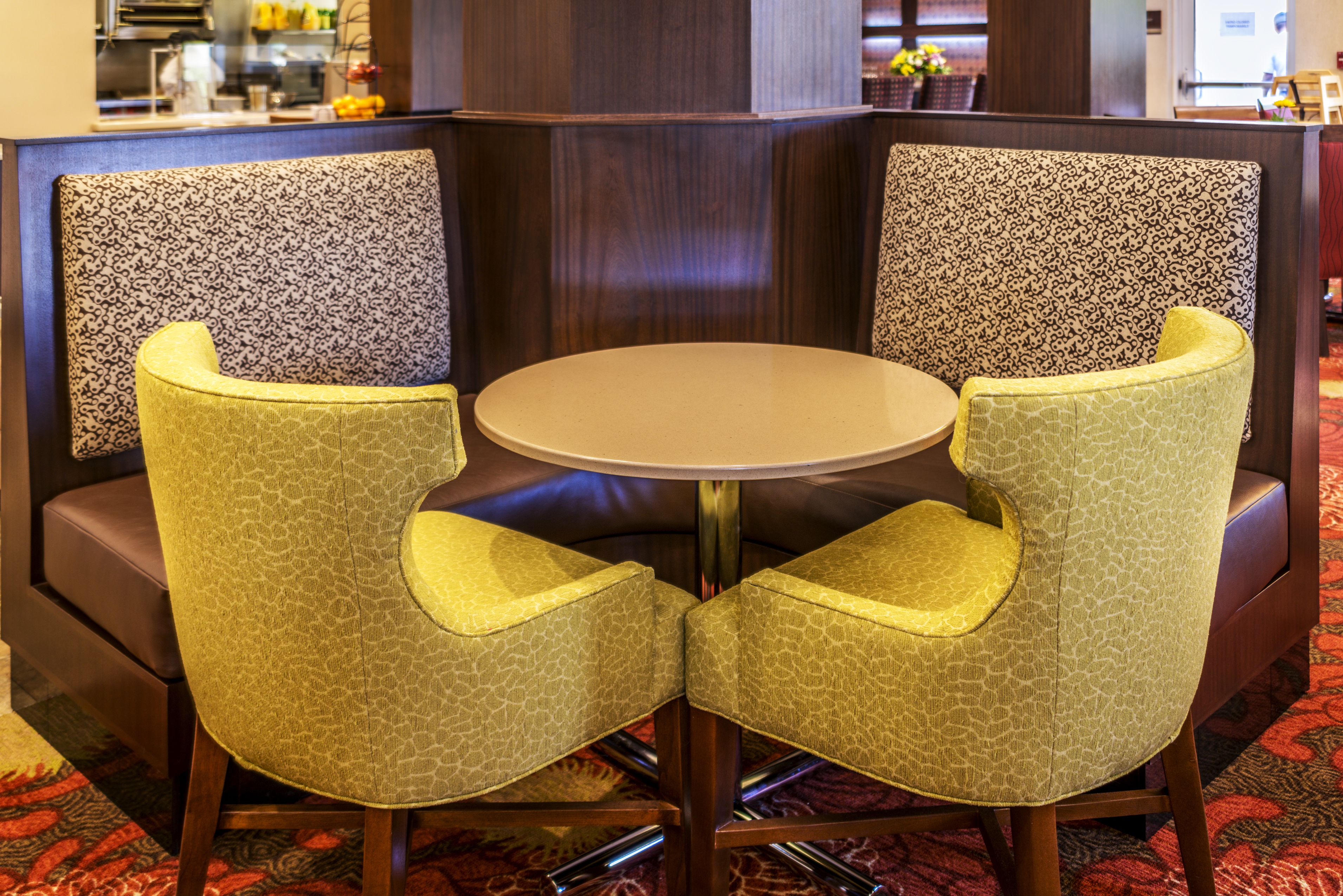 A corner seating area with two chairs and a round table, featuring patterned cushions and a wooden frame.