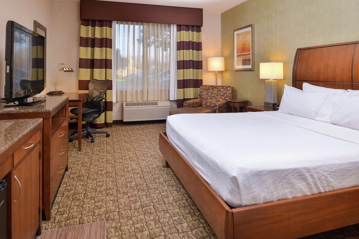 A hotel room with a bed, desk, chair, television, and a window with curtains.