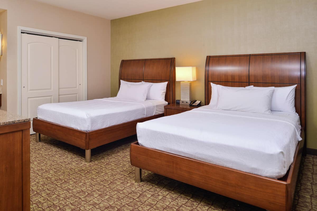 A hotel room with two wooden beds, a bedside table with a lamp, and a patterned carpet.