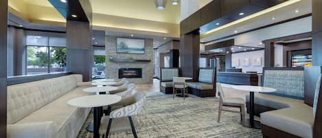 A modern lounge area with a sofa, round tables, and a fireplace.