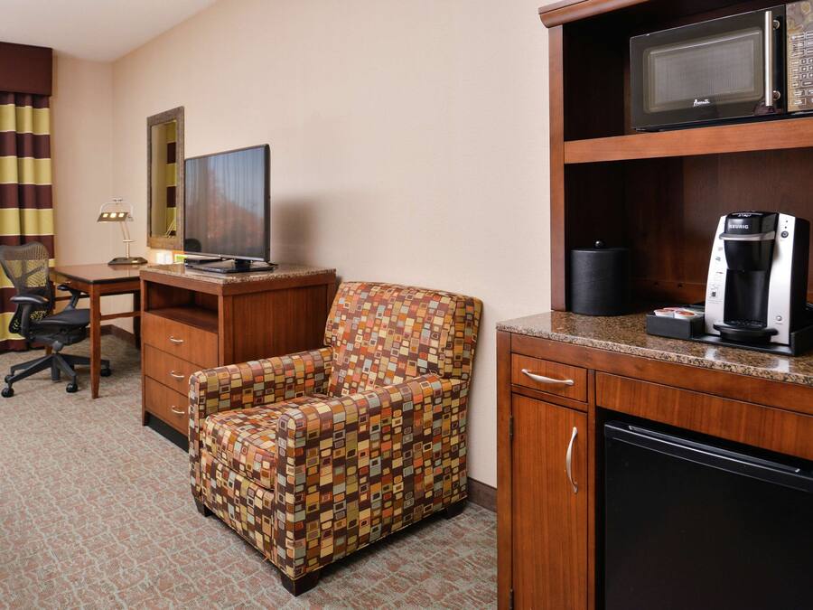 Quarto de hotel com escrivaninha, cadeira, televisão, micro-ondas, cafeteira e frigorífico.