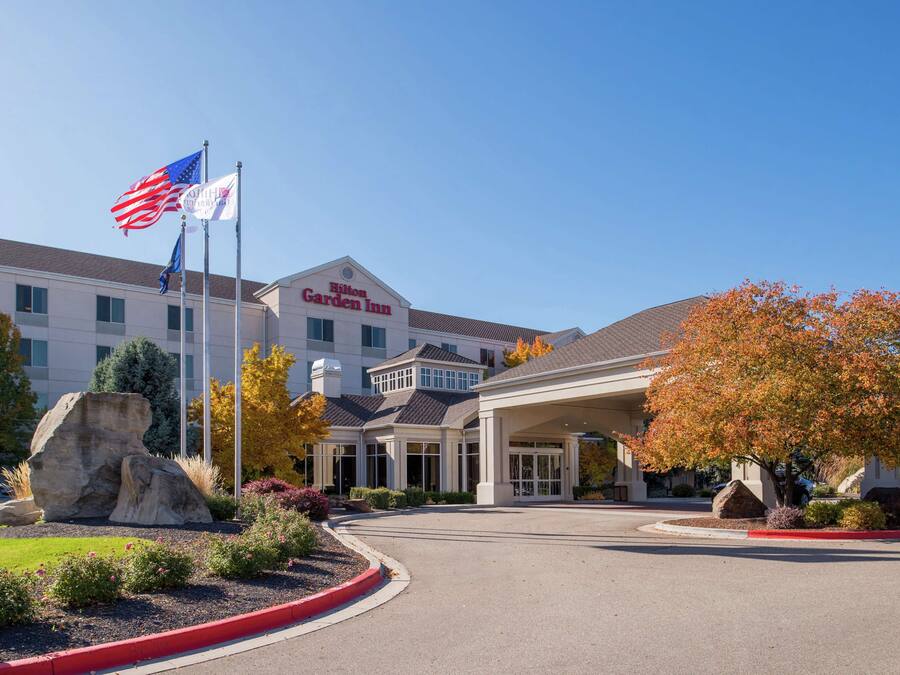 Un hotel con una entrada amplia, banderas estadounidenses y un jardín ajardinado.