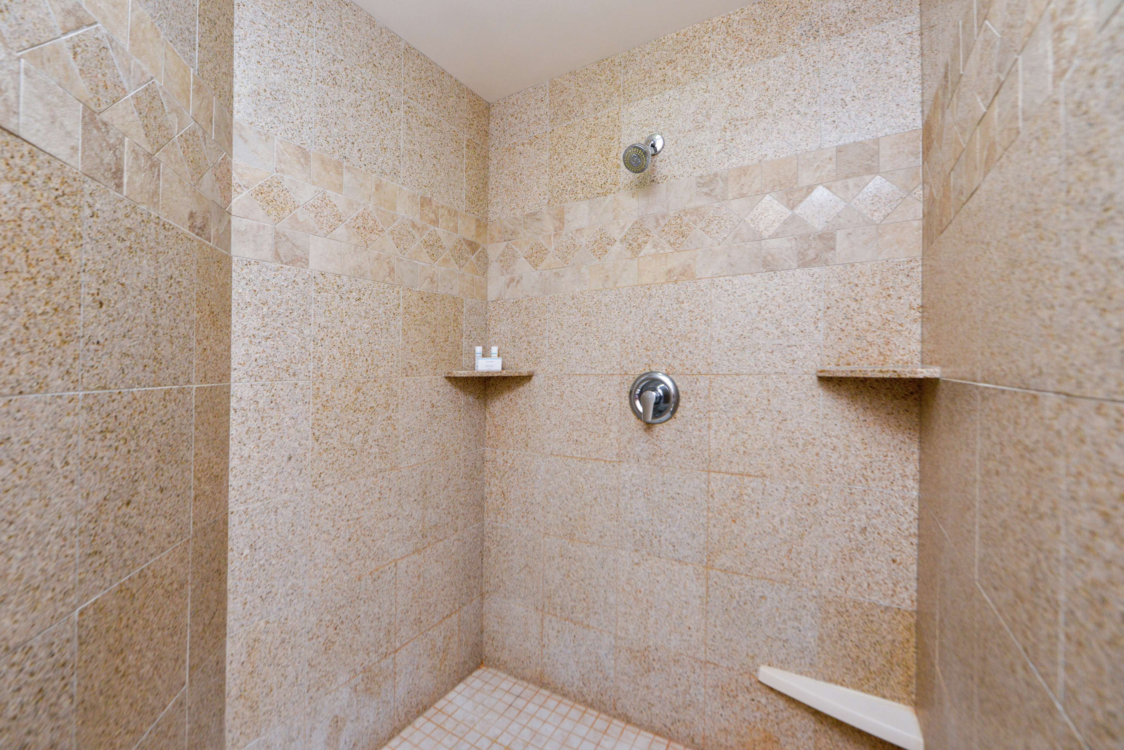 Zona de ducha con azulejos veteados y un cabezal de ducha de mano.