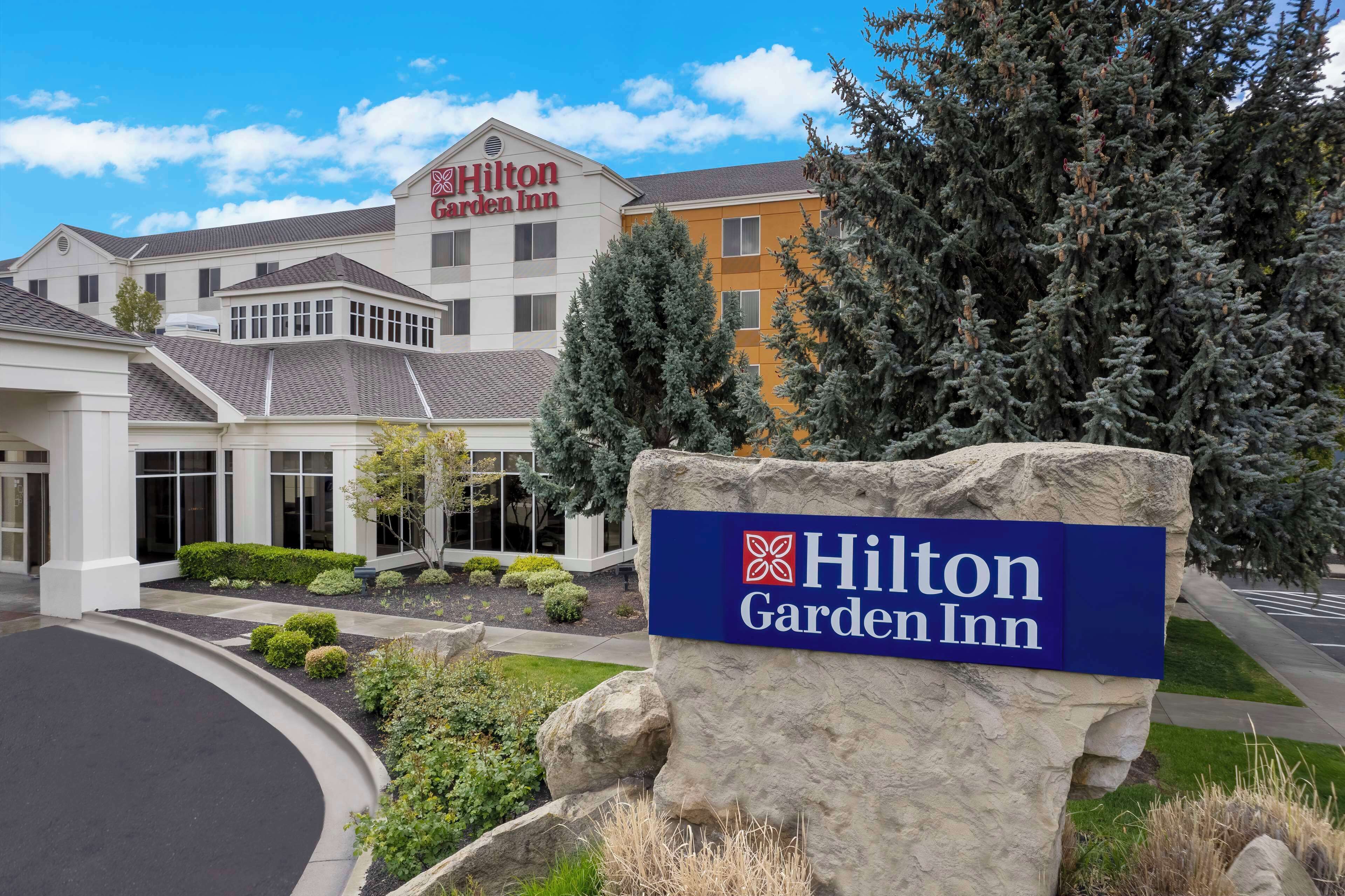 A Hilton Garden Inn with a sign in front, surrounded by landscaped areas and trees.