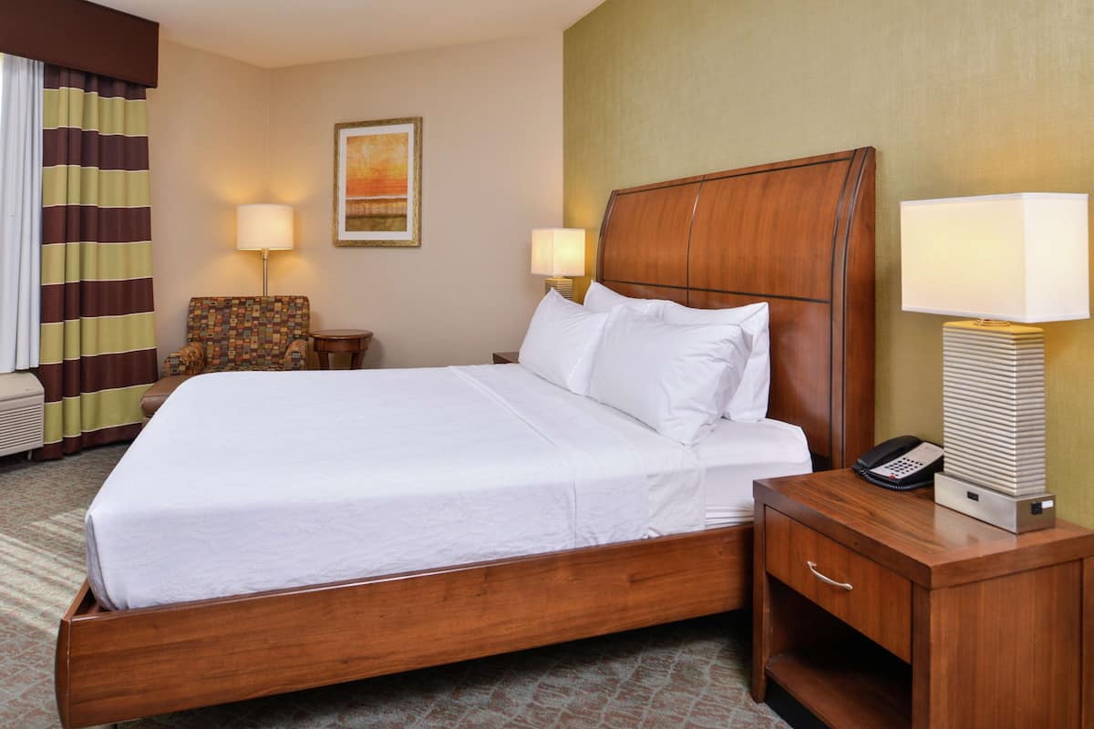A hotel room with a wooden bed, two bedside lamps, a telephone, and a chair.