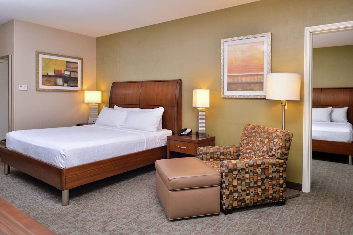A hotel room with a bed, a chair, a nightstand, and a lamp.