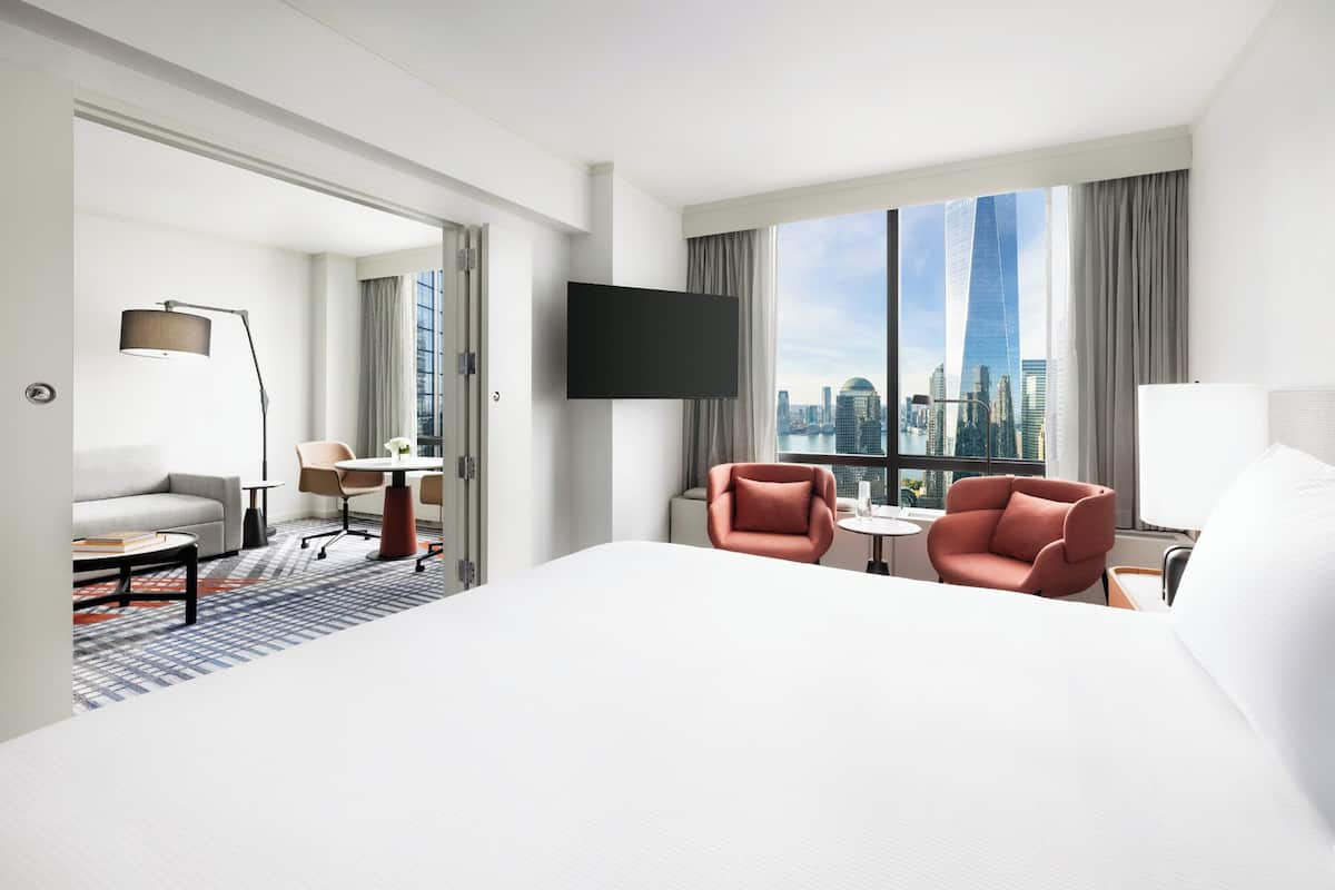 Ein Hotelzimmer mit einem großen Bett, zwei Sesseln, einem kleinen Tisch und einem Fernseher.