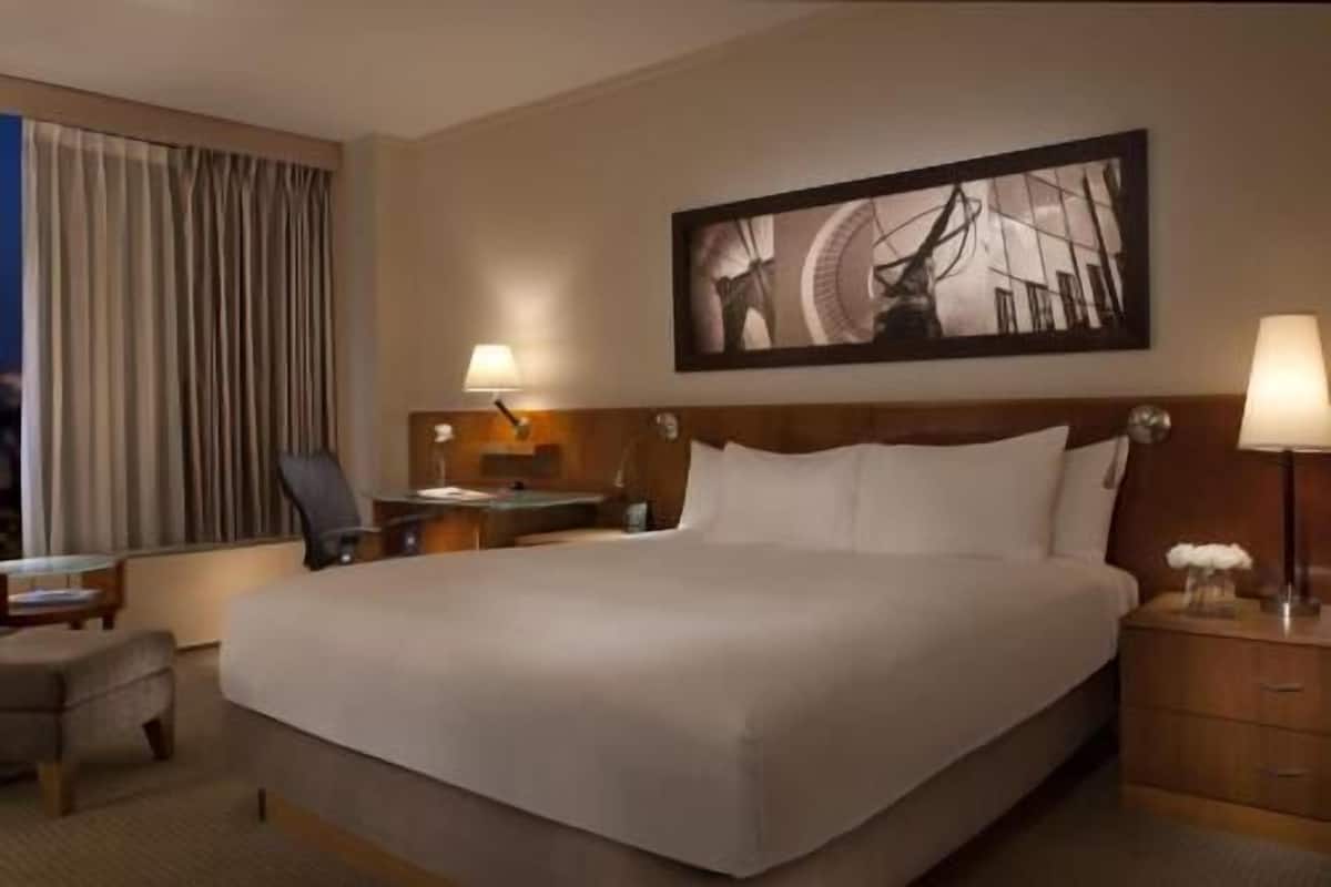 Ein Hotelzimmer mit einem großen Bett, einem Schreibtisch, einem Sessel, einem Nachttisch und einem Bild an der Wand.