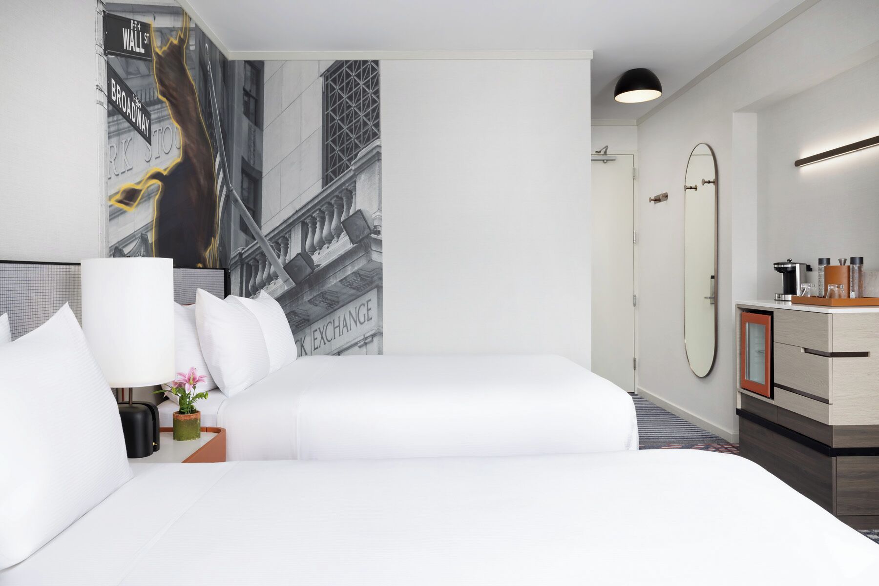 Hotelkamer met een groot bed, nachtkastje met lamp, spiegel en uitzicht op een gebouw met een bord waarop 