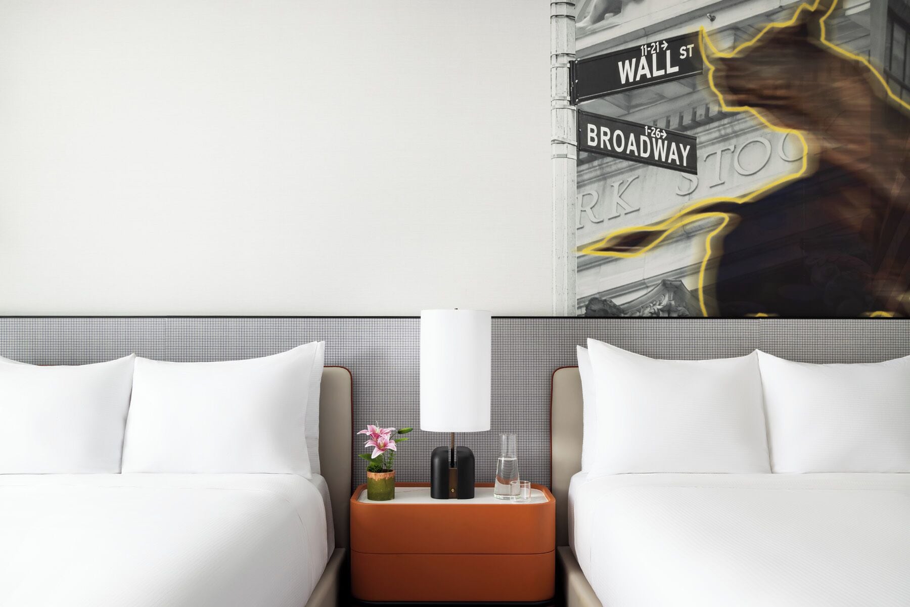 Ein Hotelzimmer mit zwei Betten, einem Nachttisch mit Lampe, einer kleinen Pflanze und einem dekorativen Wandbild.