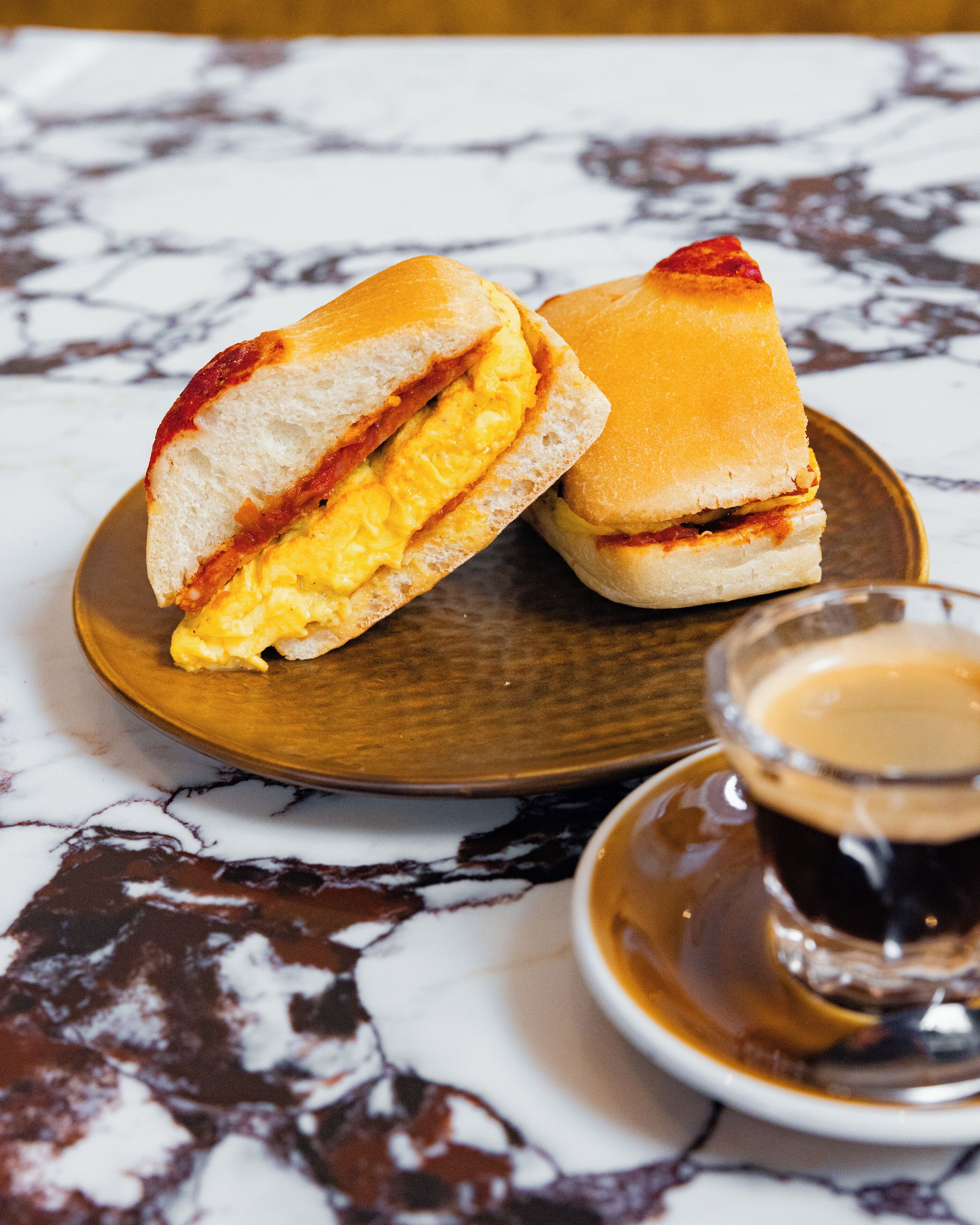 Un sandwich sur une assiette en bois, avec une tasse de café à côté.